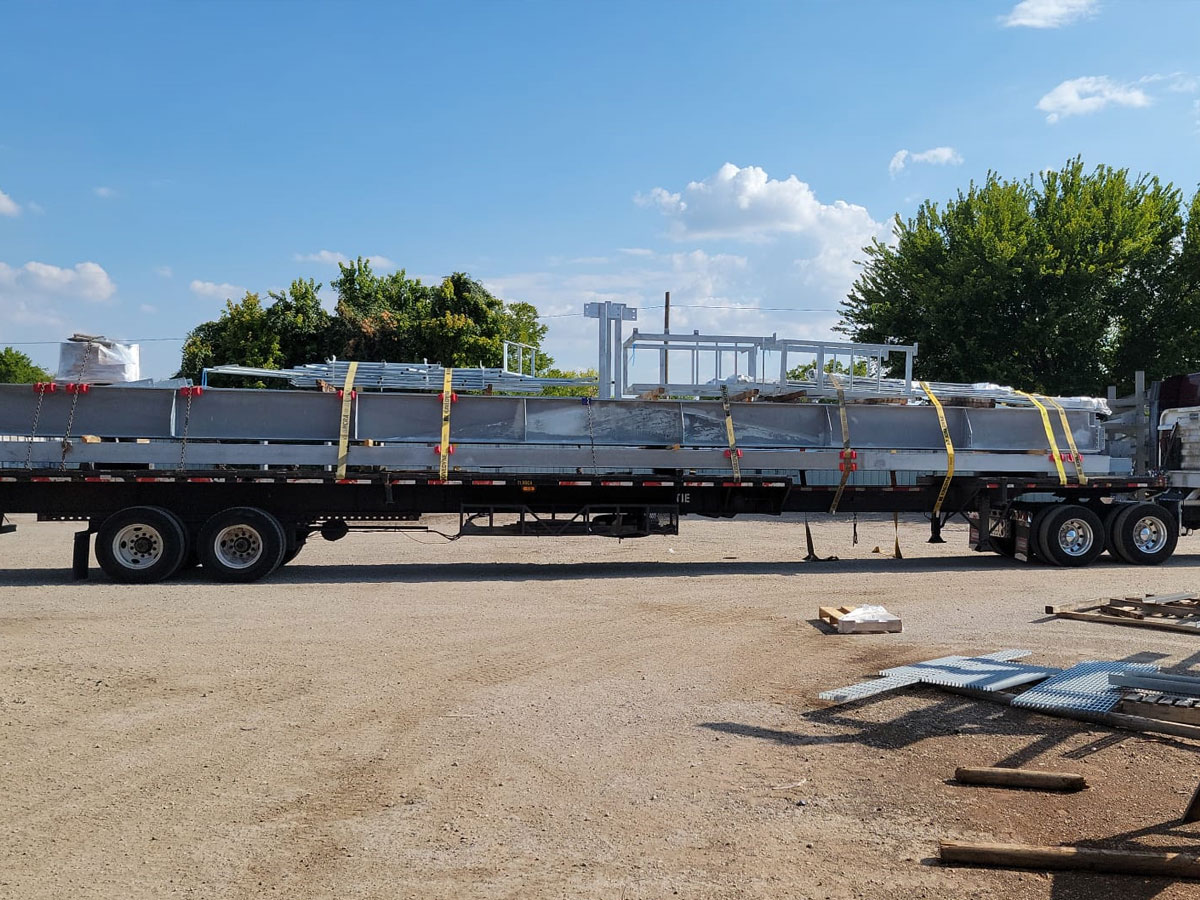 Flatbed trailer loaded with steel beams secured by straps for transport at industrial yard
