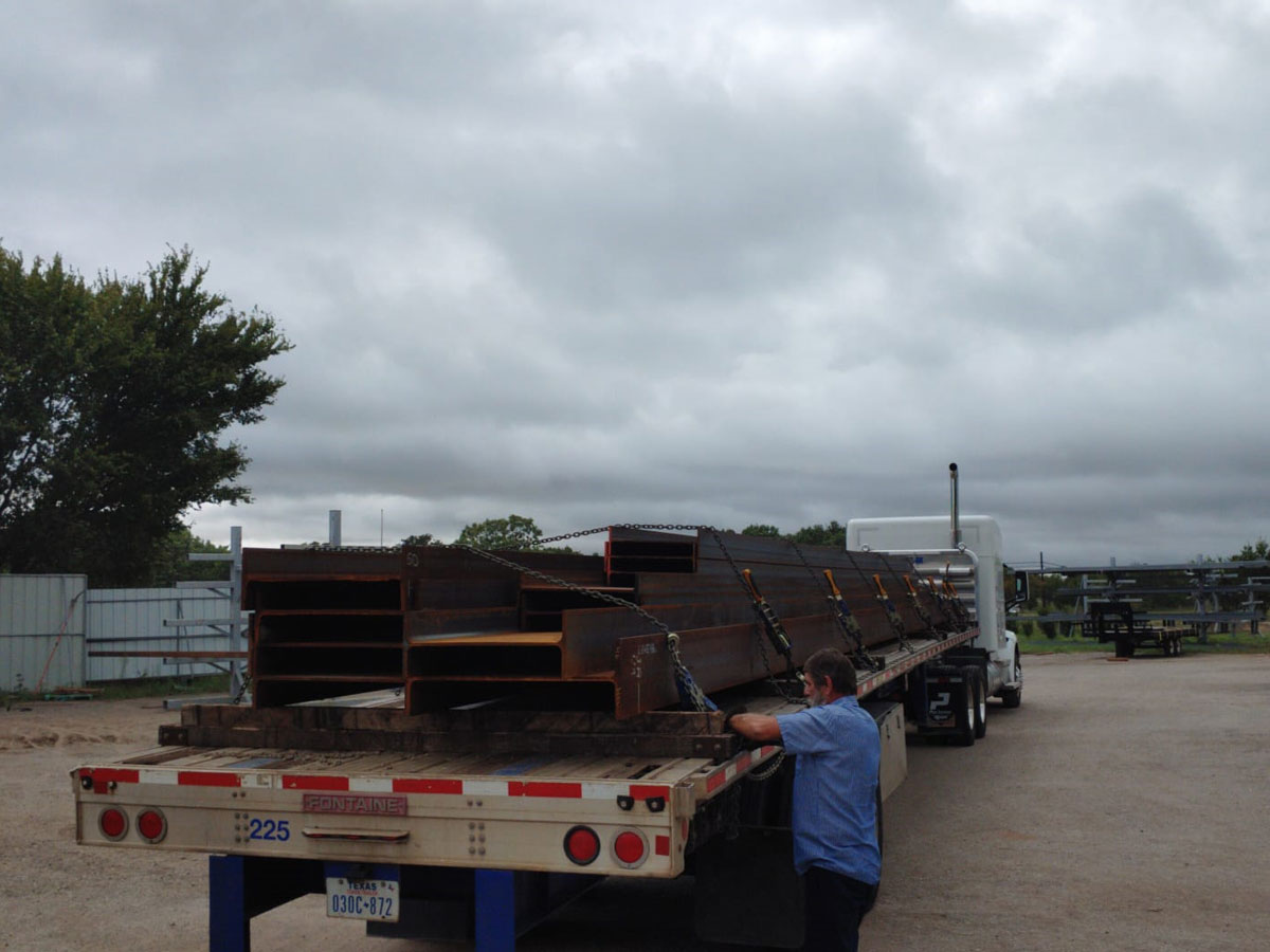 Worker securing steel I-beams on a flatbed trailer for transport