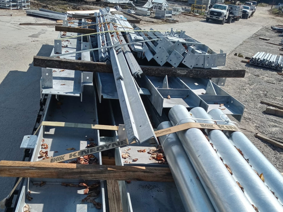Stacked galvanized steel guardrail components and posts on flatbed trailer in storage yard