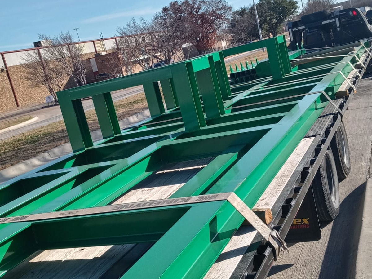 Green powder-coated steel building frames loaded on a flatbed trailer for delivery