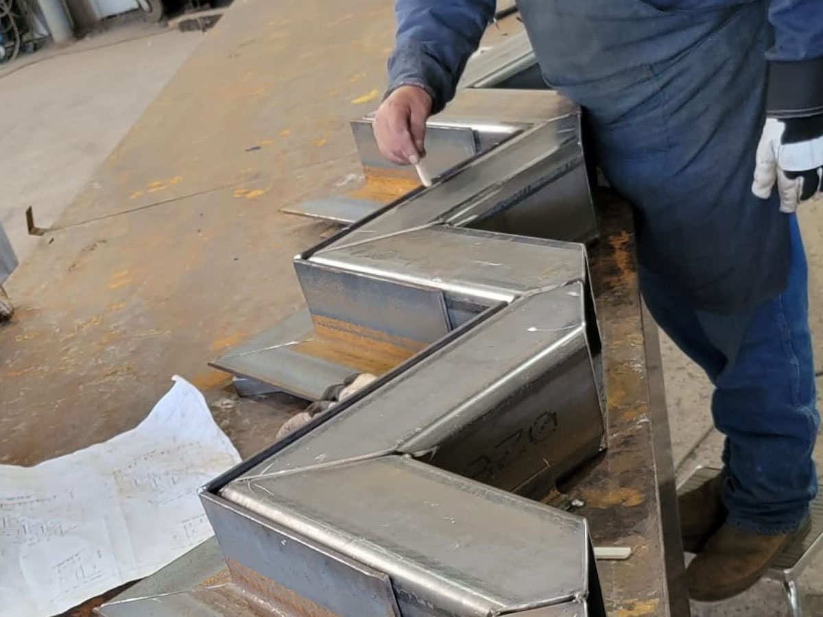 Worker marking chalk line on custom-fabricated sheet metal duct transitions on shop table
