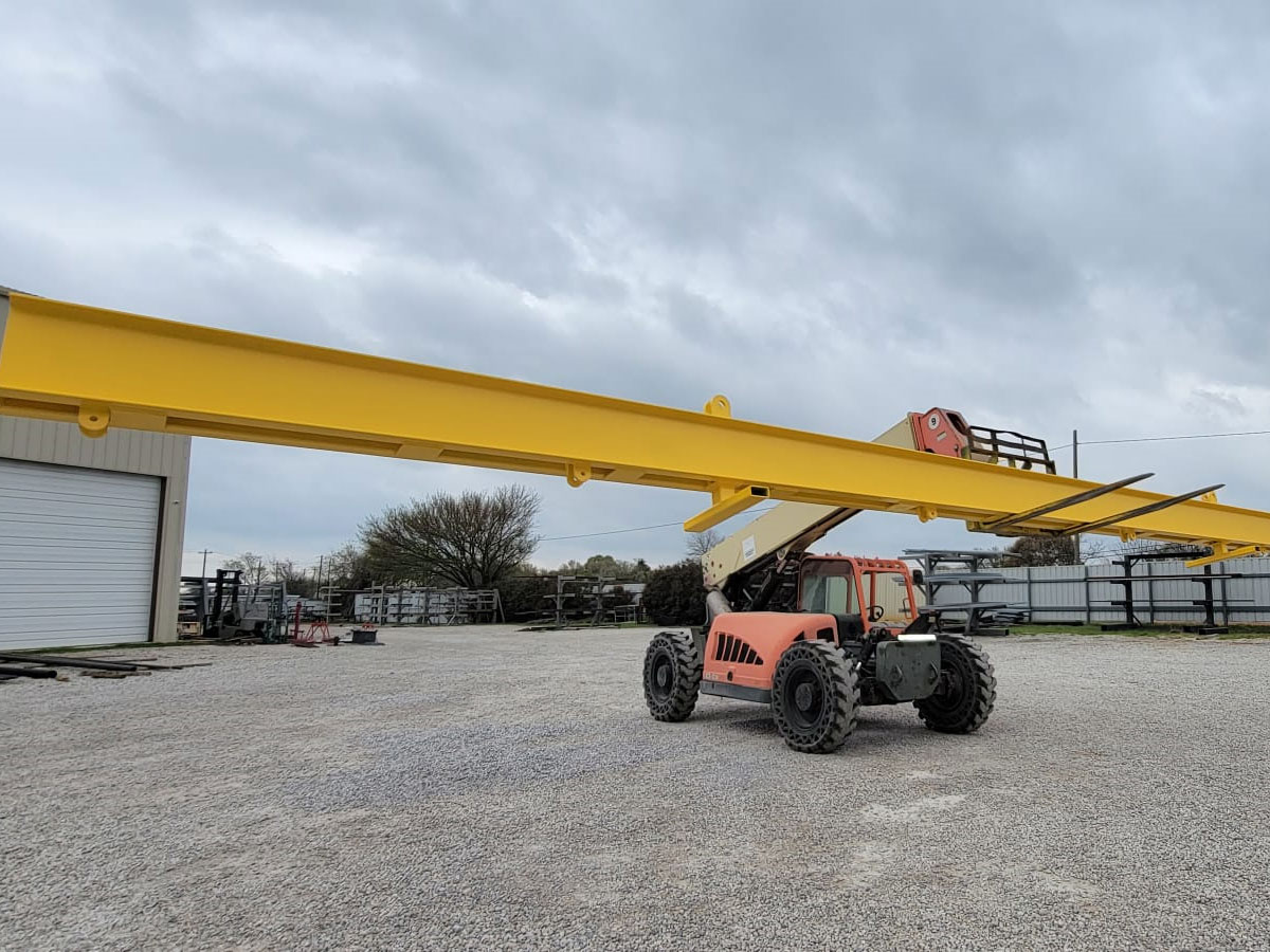 Telehandler forklift lifting a long yellow steel crane beam at an outdoor equipment yard